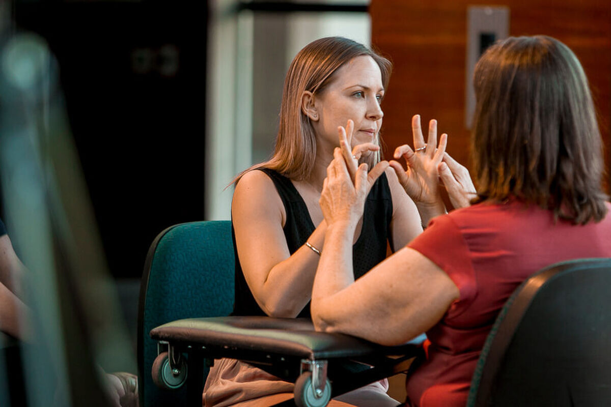 An interpreter is interpreting for a woman who is Deafblind. The interpreter signs in Auslan and the woman gently touches the interpreter's hands so she can feel what is being signed.
